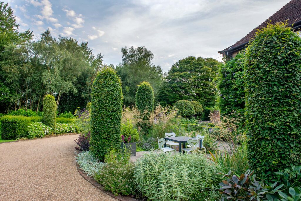 This front garden and driveway is framed by topiarised hornbeam columns and clipped hawthorn trees. These strong shapes are a great backdrop for the gentle summer planting but also provide structure and drama throughout the winter.
